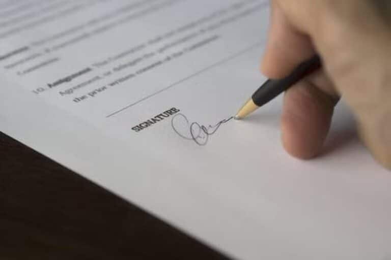 Mano firmando con un bolígrafo en la línea de firma de un documento
