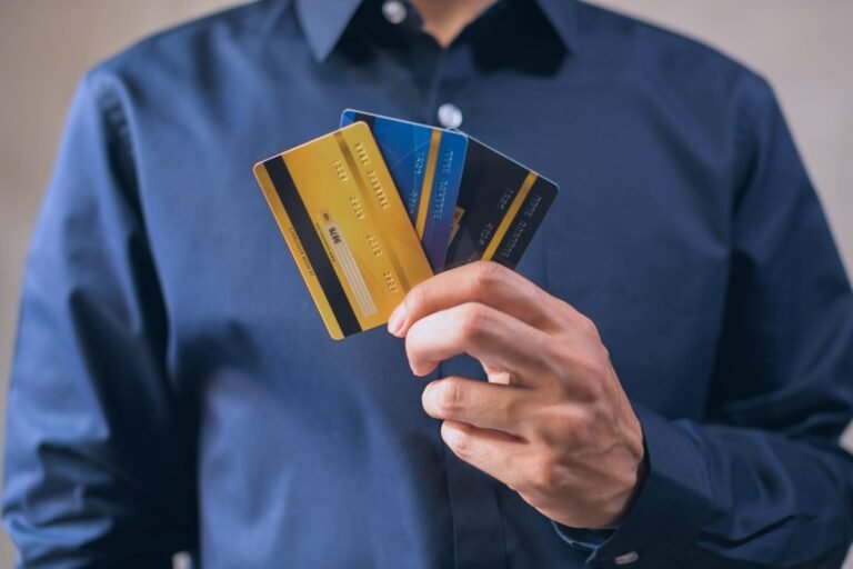 Persona con camisa azul sostiene tres tarjetas bancarias de colores en la mano